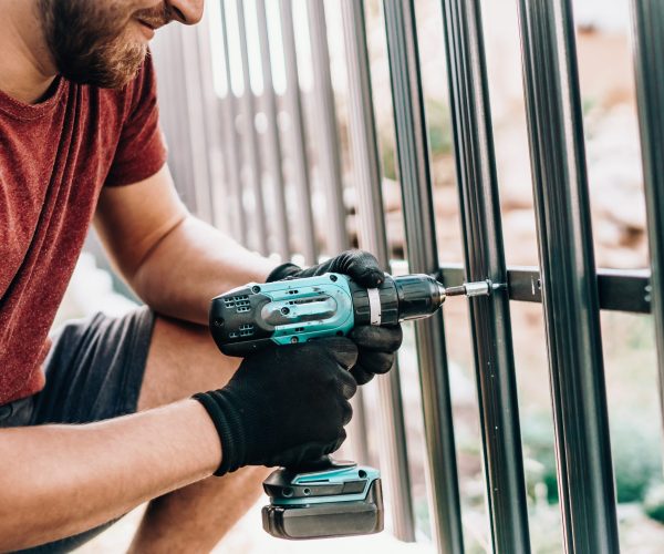 Close up portrait and details of caucasian male worker using screwdriver and screwing metal fence