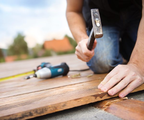 Handyman installing wooden flooring in patio, working with hammer